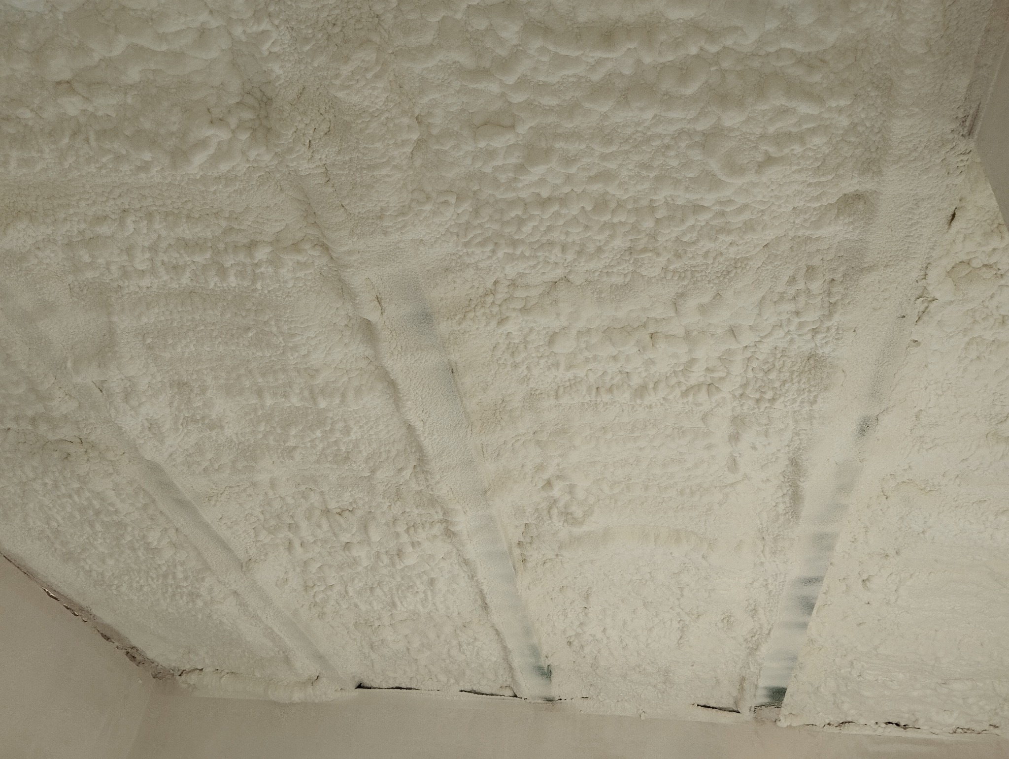 Poddasze po ociepleniu pianką poliuretanową, widoczne krokwie pokryte grubą warstwą pianki, nierównomierna struktura izolacji.