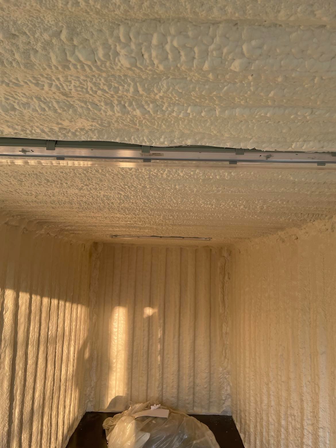 Wnętrze kontenera po natrysku pianki poliuretanowej na ściany i sufit, widoczne metalowe profile mocujące, foliowe zabezpieczenie na podłodze.