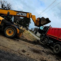 M-KOP Prace Ziemne Mateusz Sobczyk - Żółta ładowarka JCB nabiera ziemię i wysypuje ją do czerwonej ciężarówki na placu budowy, pochmurne niebo w tle.