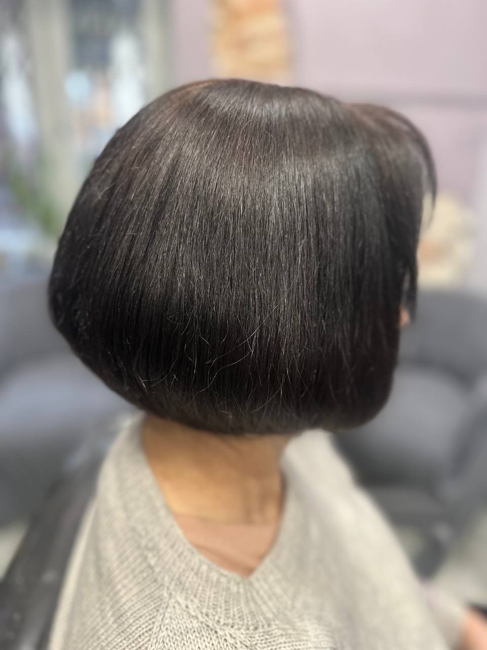 Krótkie, gładkie, ciemne włosy z tyłu głowy, widoczne delikatne cieniowanie, sweter z dzianiny w tle rozmyte meble salonu.