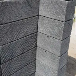 Fragment elewacji z ciemnoszarych, teksturowanych płyt kamiennych ułożonych w narożniku, z widoczną osobą w tle.