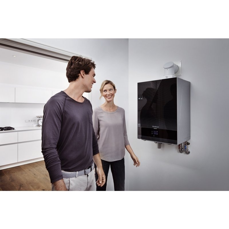 Para podziwia nowoczesny, wiszący kocioł grzewczy Buderus w minimalistycznym wnętrzu, z widocznymi rurami i elektronicznym wyświetlaczem.