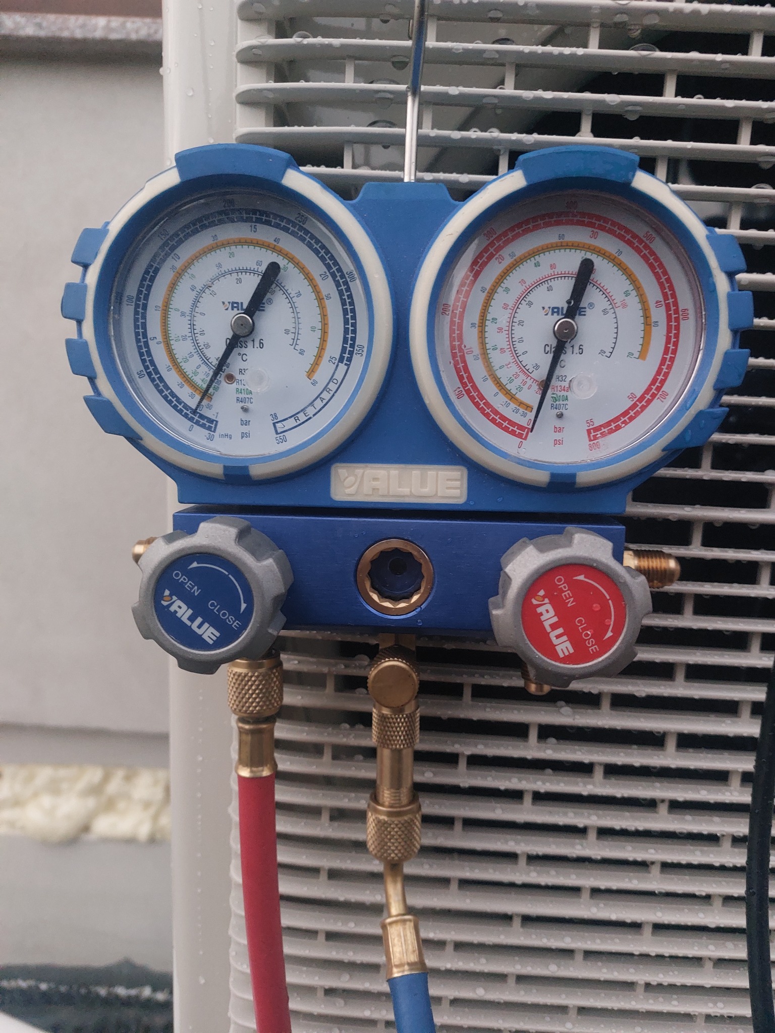 Manometry z podłączonymi przewodami na tle białej obudowy urządzenia, prawdopodobnie klimatyzacji, z widocznymi kroplami wody.