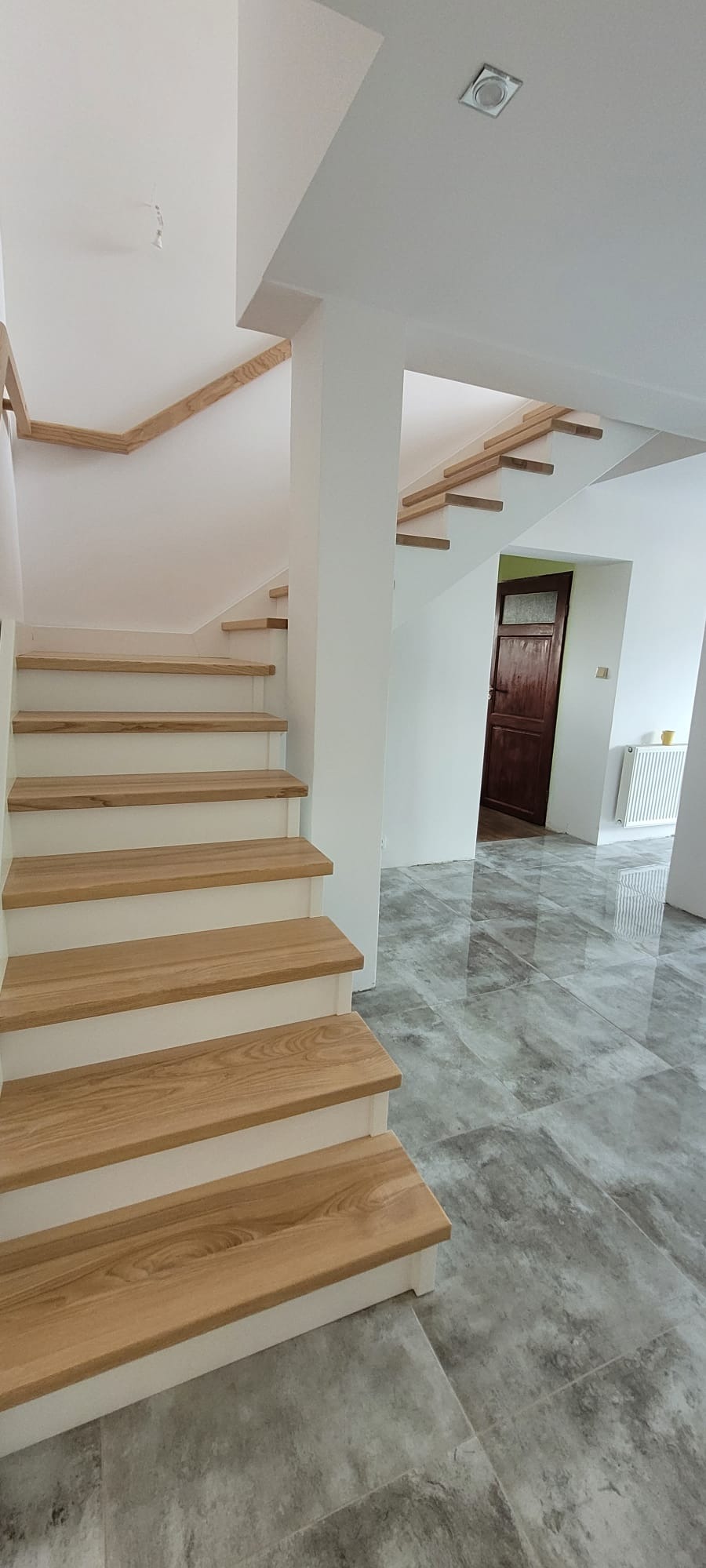 Nowoczesne schody drewniane z białymi podstopnicami i dębowymi stopniami na tle szarej podłogi. Widoczne wykończenie i detale.