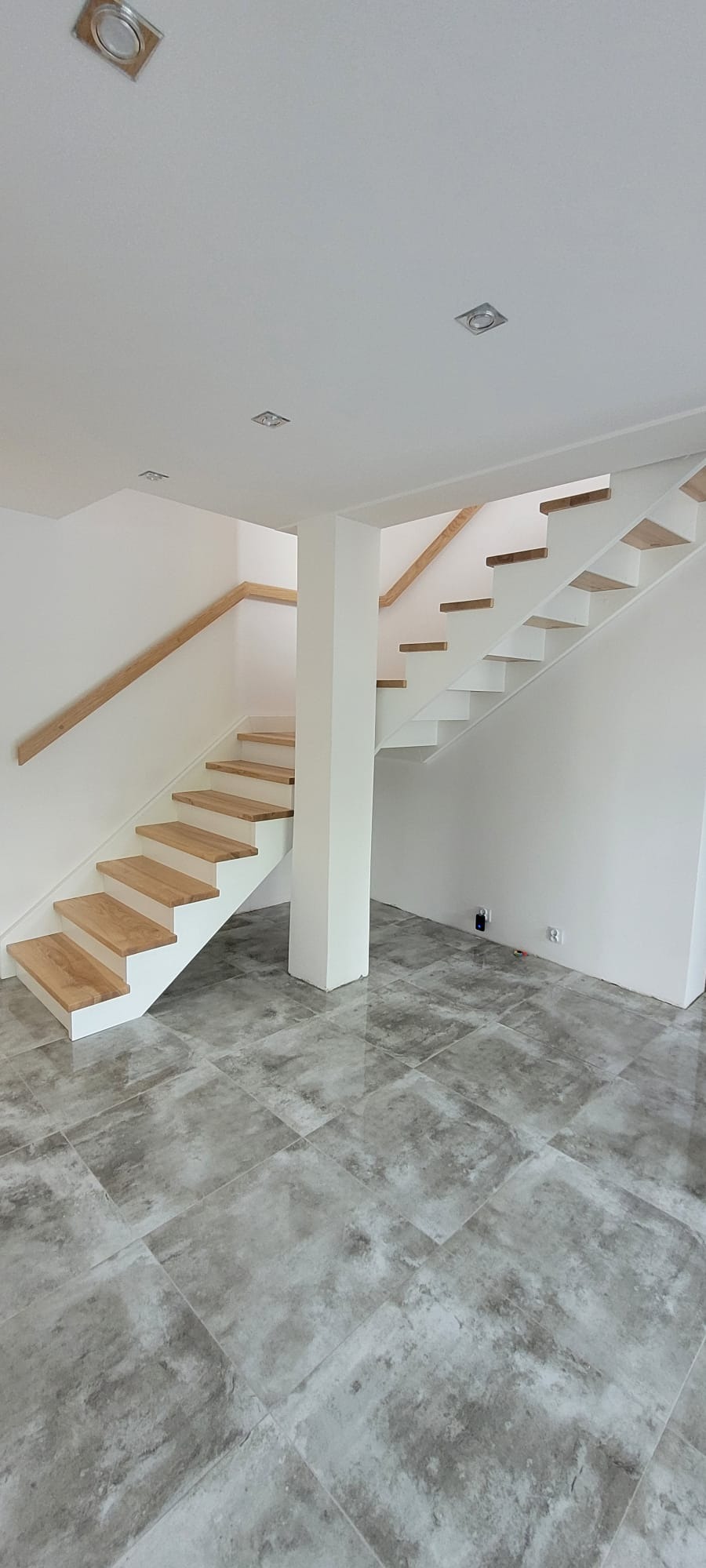 Nowoczesne schody z drewnianymi stopniami i białymi policzkami, bez balustrady, w jasnym wnętrzu z szarą podłogą. Minimalistyczny design, widok z dołu.