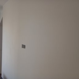 REHA-BUD SPÓŁKA Z OGRANICZONĄ ODPOWIEDZIALNOŚCIĄ - Świeżo pomalowana ściana w jasnym odcieniu z przygotowanym otworem na gniazdko elektryczne, widoczny fragment grzejnika i okna.