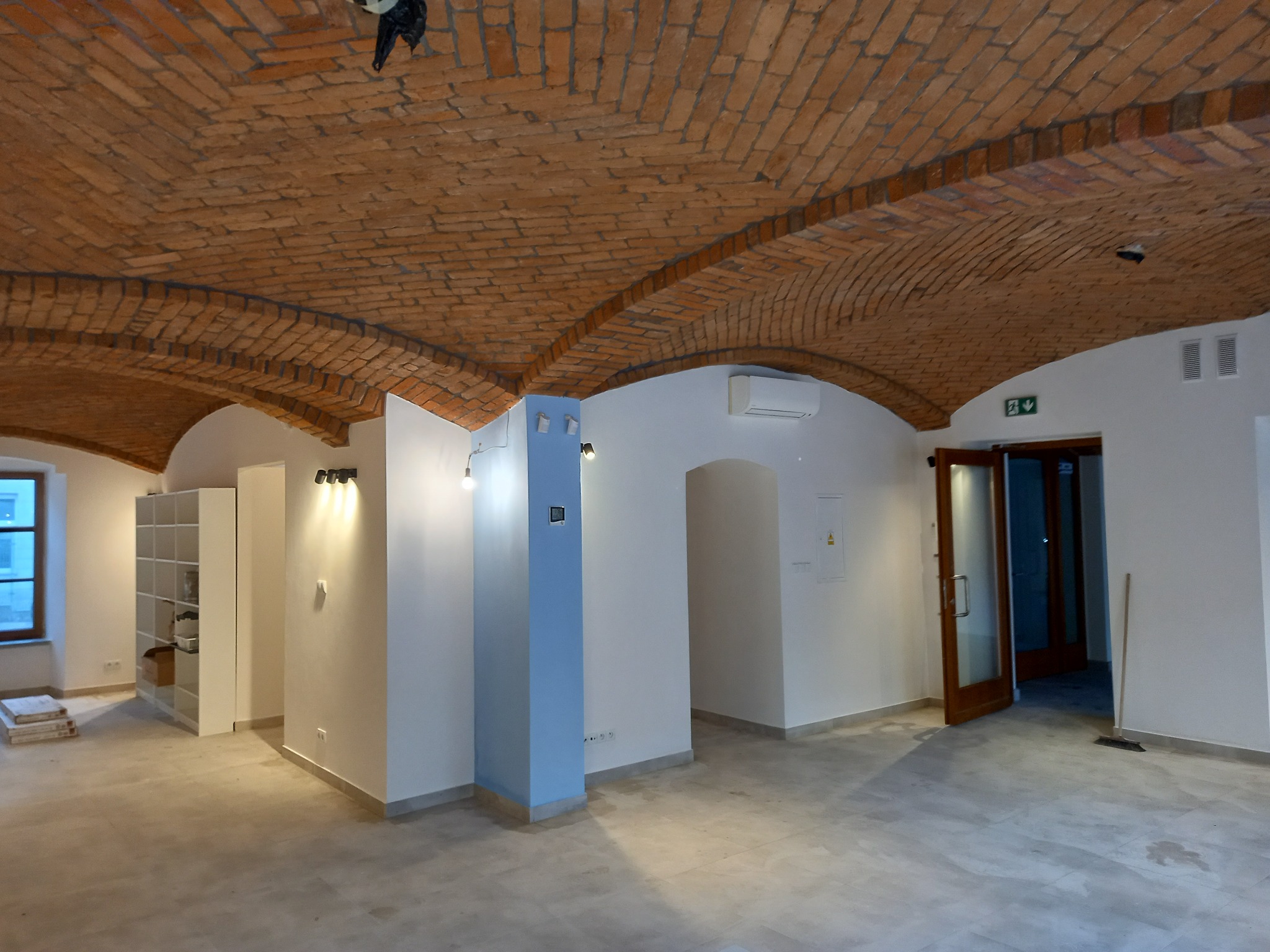 Przestronne wnętrze biurowe z charakterystycznym sklepieniem łukowym z cegły, świeżo pomalowane ściany w odcieniach bieli, jasna podłoga i elementy wykończeniowe w szarościach, widoczny...