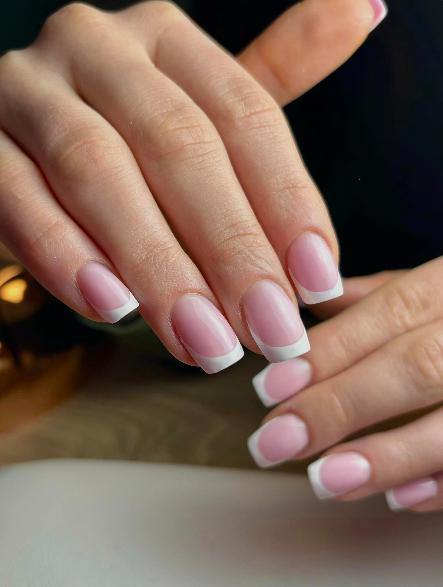 Dłonie z perfekcyjnym manicure francuskim, delikatny różowy lakier i idealnie białe końcówki, widoczne detale skóry i precyzja wykonania.