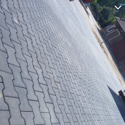 HubMar - Ułożona szara kostka brukowa w kształcie litery H prowadząca w kierunku ceglanego budynku z małym oknem.