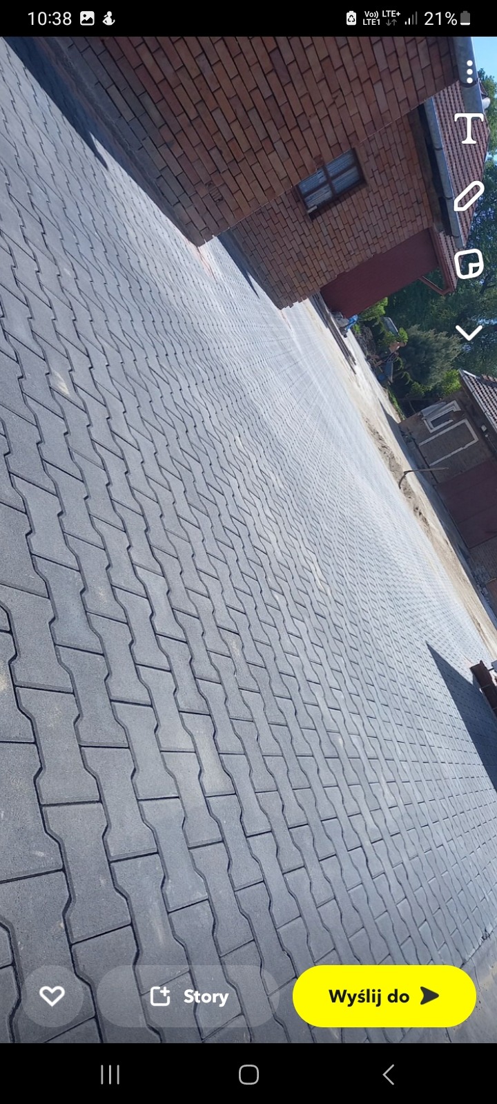 Ułożona szara kostka brukowa w kształcie litery H prowadząca w kierunku ceglanego budynku z małym oknem.