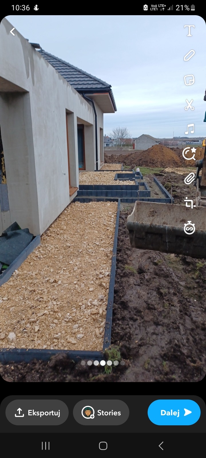 Przygotowanie podłoża z kruszywa pod ścieżkę wokół domu, widoczne obrzeża i wykopana ziemia, w tle budynek w stanie surowym.