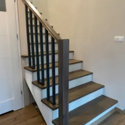 Nowoczesne schody drewniane z ciemnymi stopniami i czarnymi, prostymi balustradami, białe podstopnice, widok z dołu na górę.