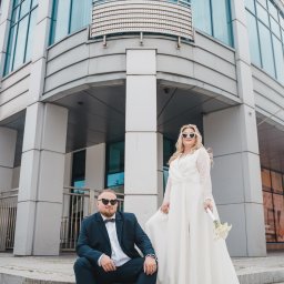 NATS PHOTOGRAPHY Natalia Głowacka - Para młoda w okularach w kształcie serc pozuje na schodach nowoczesnego budynku z przeszkloną fasadą.