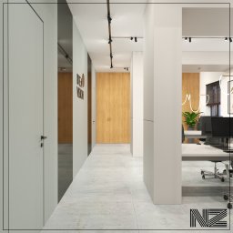 NZ PROJEKT & WNĘTRZE Nicole Znajmiecka - Nowoczesne biuro z jasnymi ścianami, drewnianymi akcentami i minimalistycznym oświetleniem szynowym, widok na stanowiska pracy z roślinami doniczkowymi i logo firmy na ścianie.