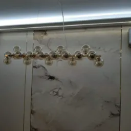 Nowoczesny żyrandol z kulistymi kloszami w odcieniach bursztynu, zawieszony na tle ściany z marmurowym wzorem i listwą LED pod sufitem.