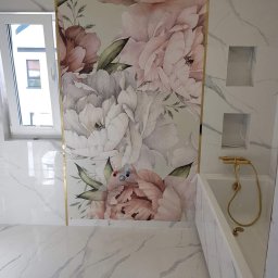 14 - Wykończona łazienka z marmurowymi płytkami, dekoracyjną tapetą w kwiaty z złotymi listwami, białą wanną i złotą armaturą oraz wnękami w ścianie.