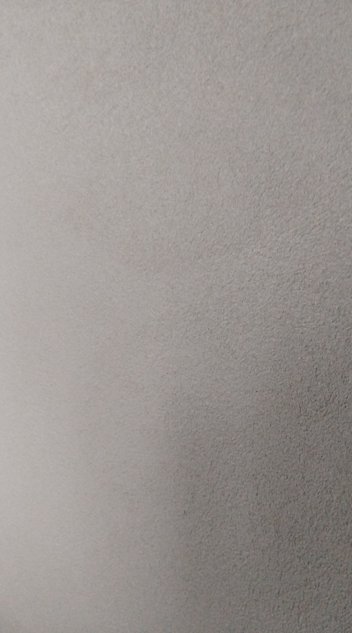 Szara, jednolita powierzchnia z delikatną fakturą, przypominająca świeżo nałożony tynk lub gładź. Oświetlenie z lewej strony tworzy subtelny gradient.