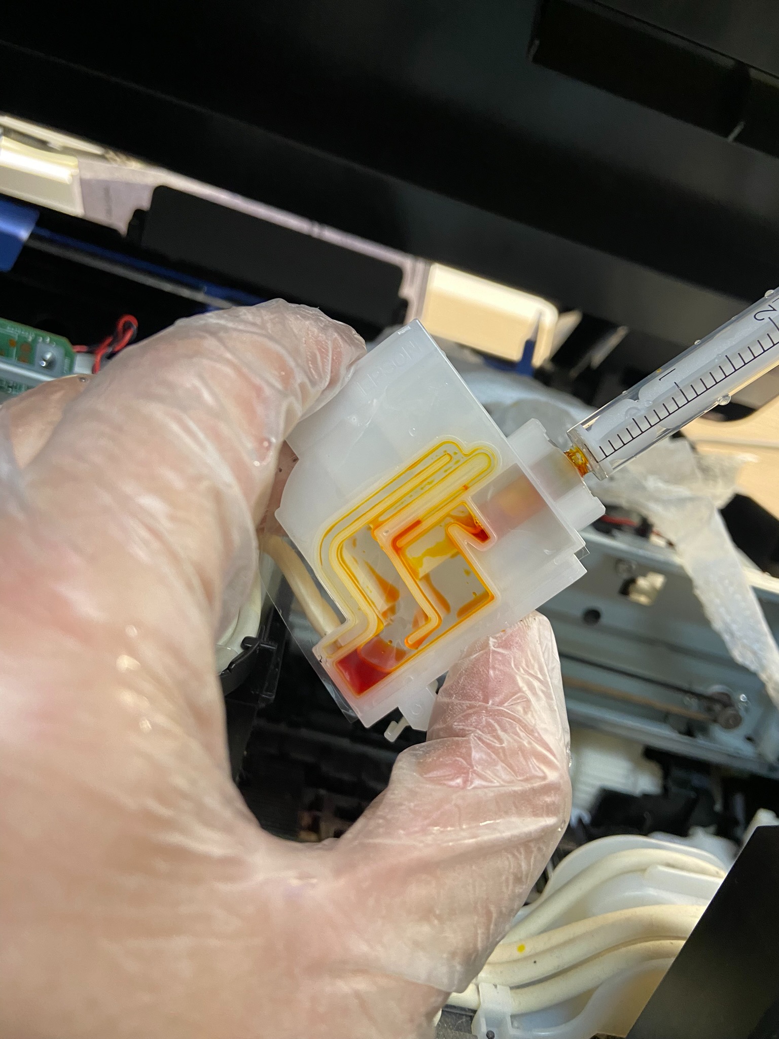 Uzupełnianie pojemnika z tuszem koloru żółtego za pomocą strzykawki wewnątrz drukarki przez osobę w rękawiczce ochronnej.