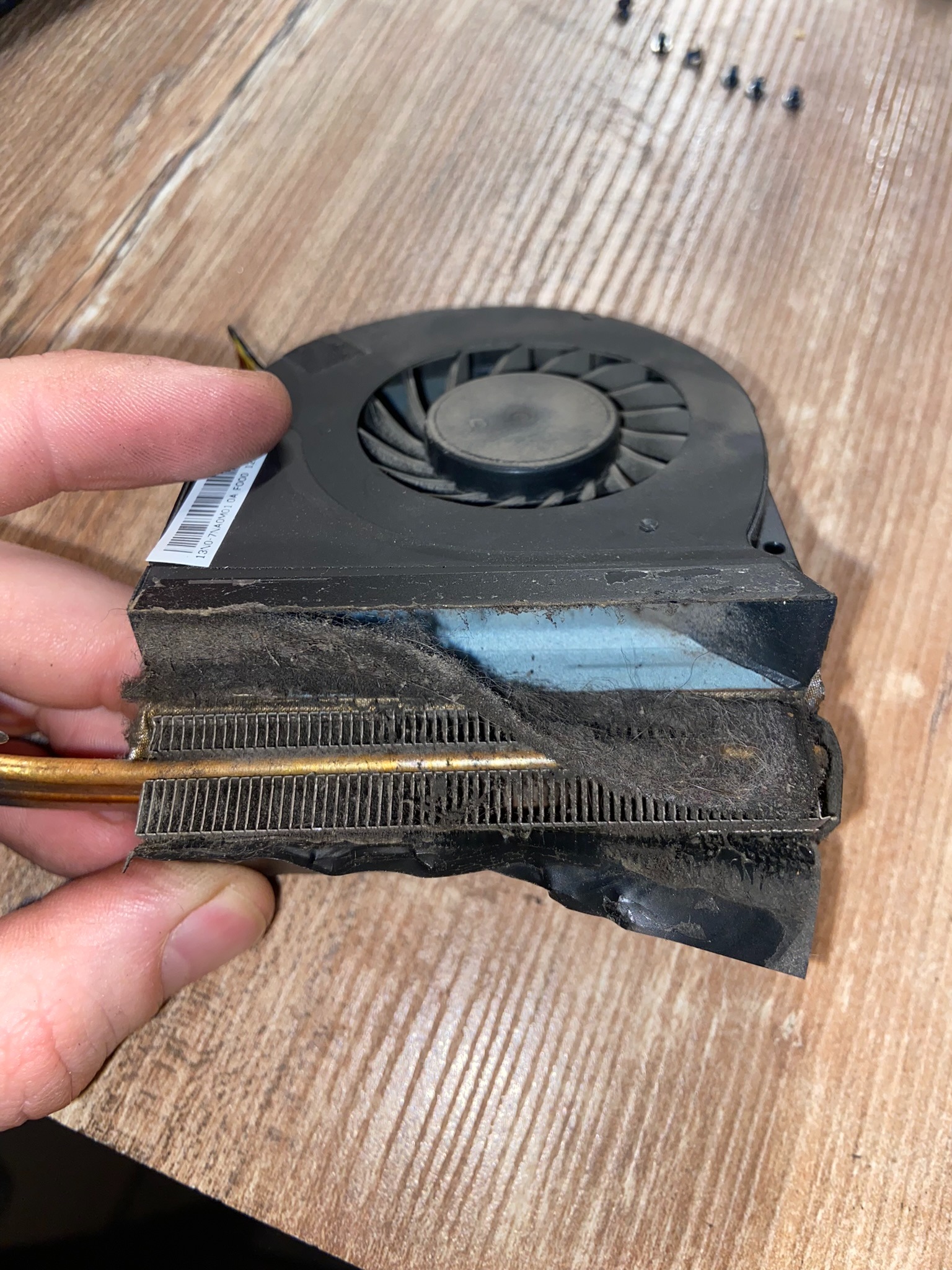 Zanieczyszczony radiator z wentylatorem od laptopa trzymany w dłoni, widoczne nagromadzenie kurzu i brudu na żebrach radiatora i wentylatorze.