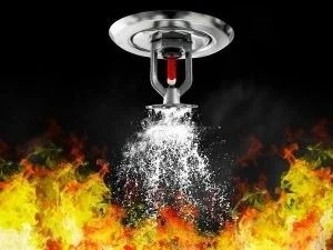 Dysza tryskacza przeciwpożarowego uruchomiona, rozpylająca wodę na tle płomieni.