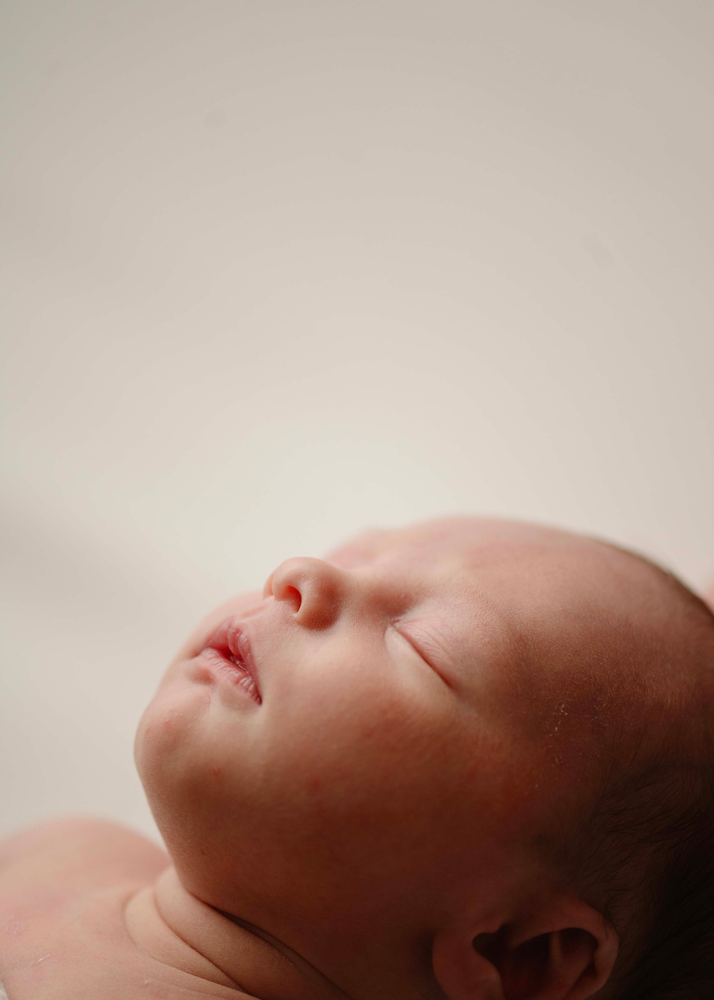 Śpiący noworodek, zbliżenie na twarz z delikatnym oświetleniem, widoczne drobne włoski na głowie dziecka.