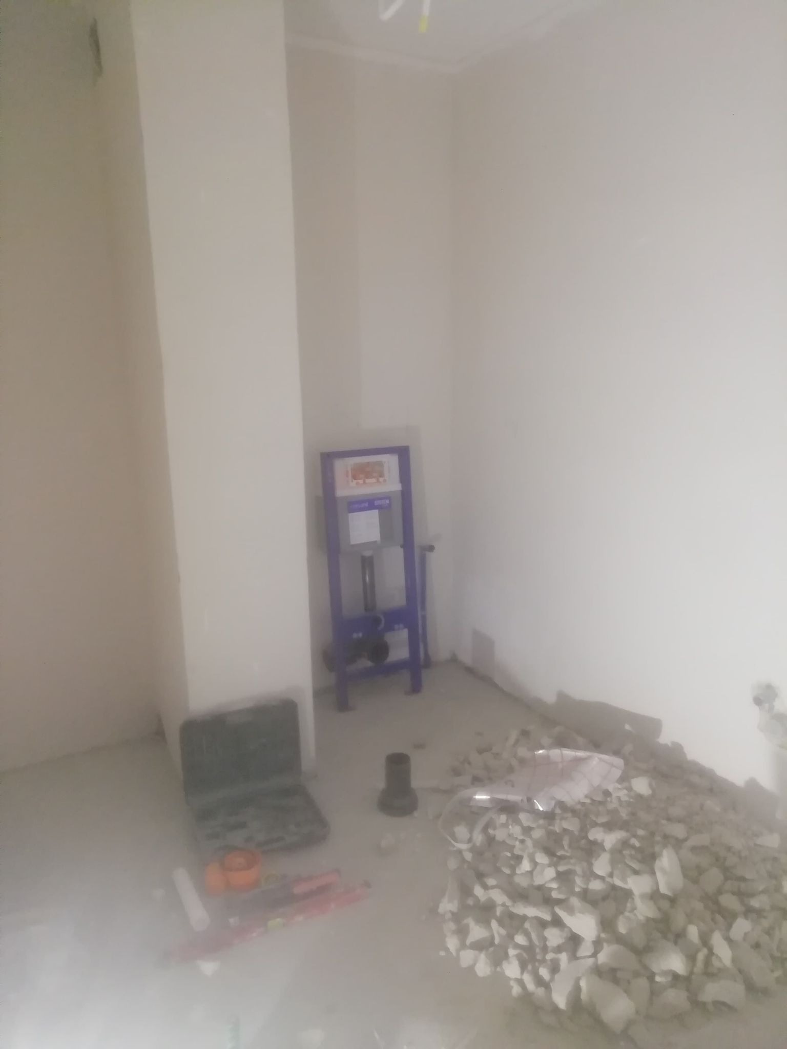 Wnętrze łazienki w trakcie remontu: stelaż podtynkowy WC, narzędzia, gruz i przygotowane ściany pod wykończenie.