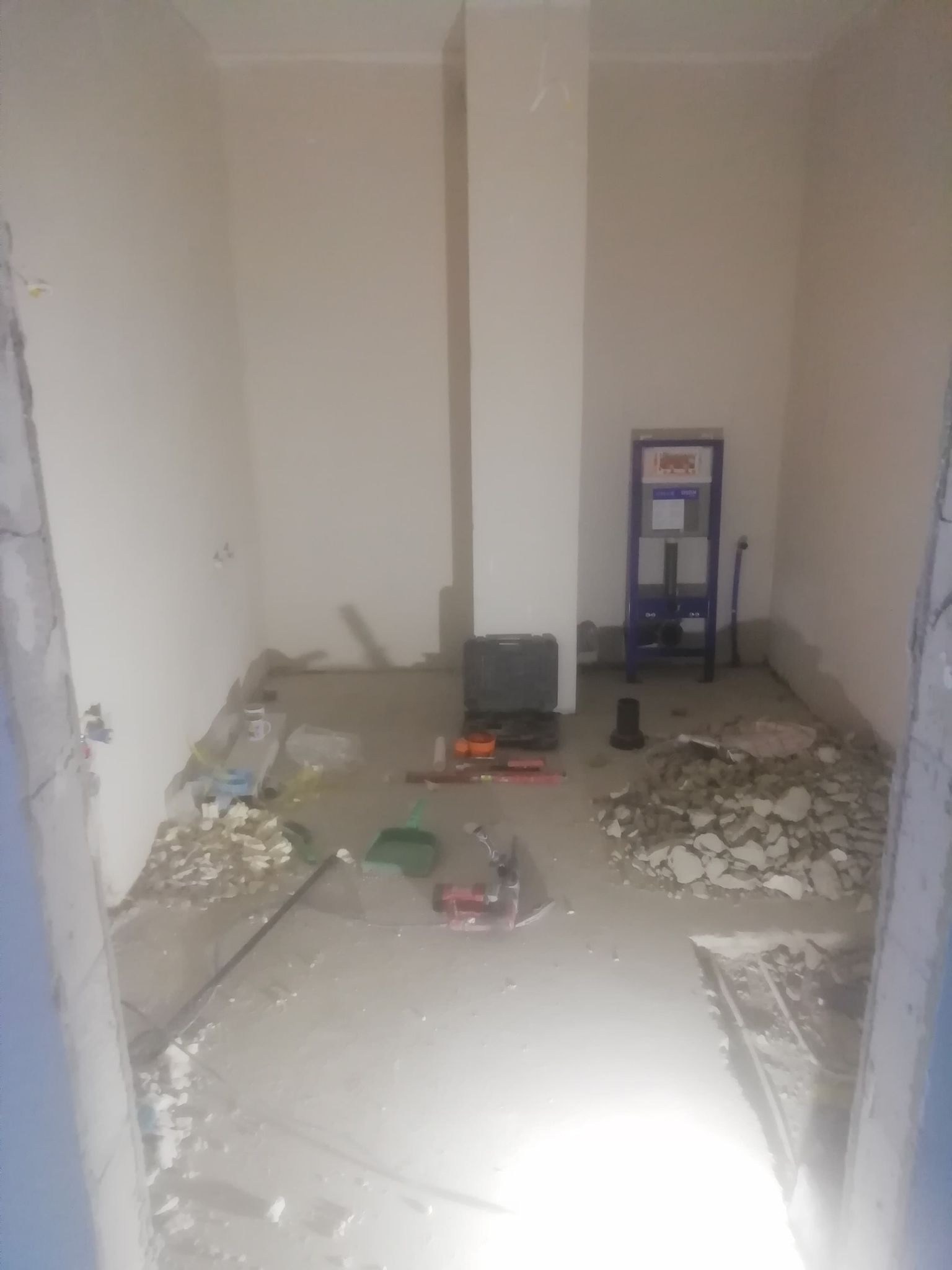 Łazienka w trakcie demontażu: widoczne gruz, narzędzia, stelaż podtynkowy WC, ściany przygotowane do dalszych prac.