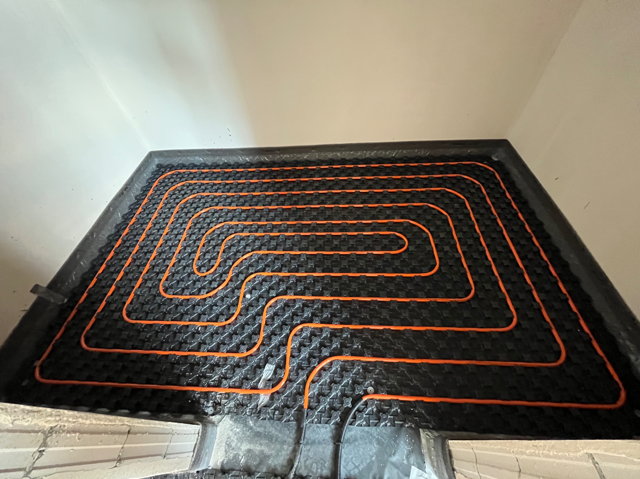 Pomarańczowe rury w systemie podłogowym na czarnej macie izolacyjnej, widoczne kable elektryczne, przygotowane do wylewki.