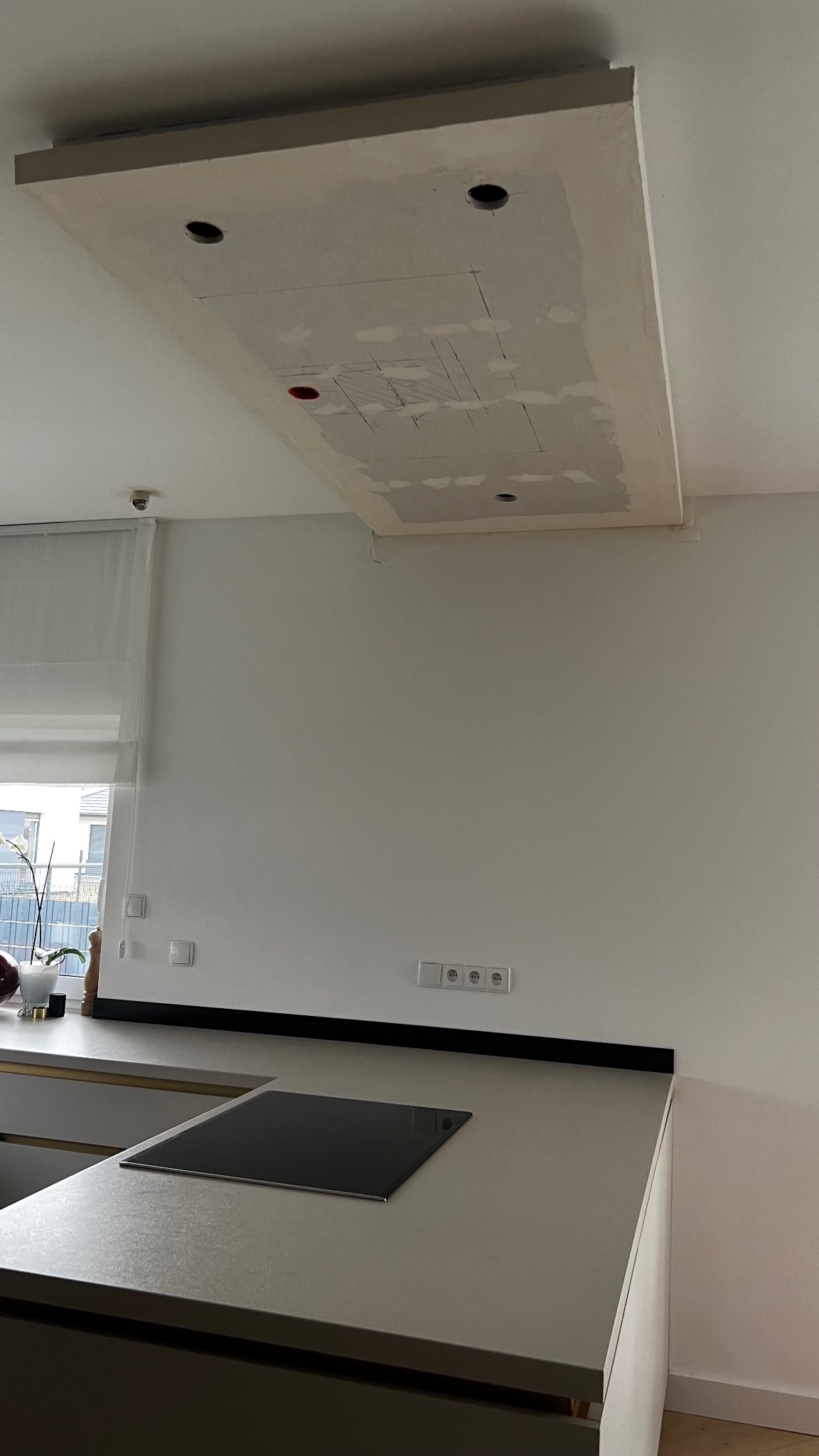 Wnętrze kuchni w trakcie remontu, widoczny sufit podwieszany z otworami na oświetlenie, częściowo wykończony, z widocznymi śladami szpachlowania i zaznaczonymi liniami podziału.