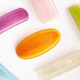 La vue - Fotografia produktowa: Różnokolorowe, błyszczące spinki do włosów ułożone na białym tle, widoczne z góry.