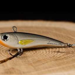 La vue - Szaro-pomarańczowa przynęta spinningowa z żółtym akcentem, leżąca na drewnianym blacie z widocznym podpisem 'Dreamy 124'.