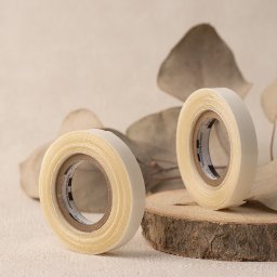 La vue - Dwie rolki taśmy dwustronnej na drewnianym krążku, z suszonymi liśćmi eukaliptusa w tle, na beżowej powierzchni.