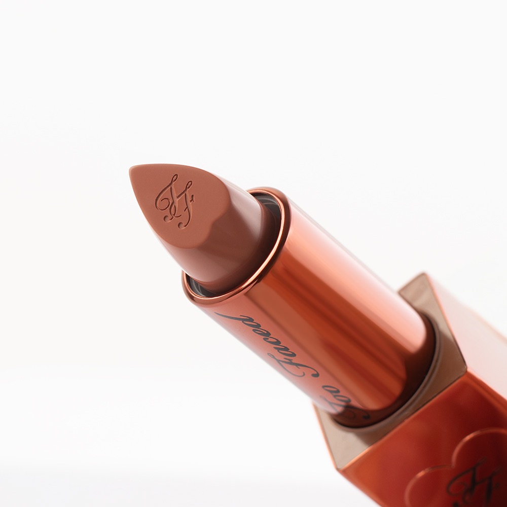 Beżowa szminka Too Faced z wytłoczonym logo na tle bieli.