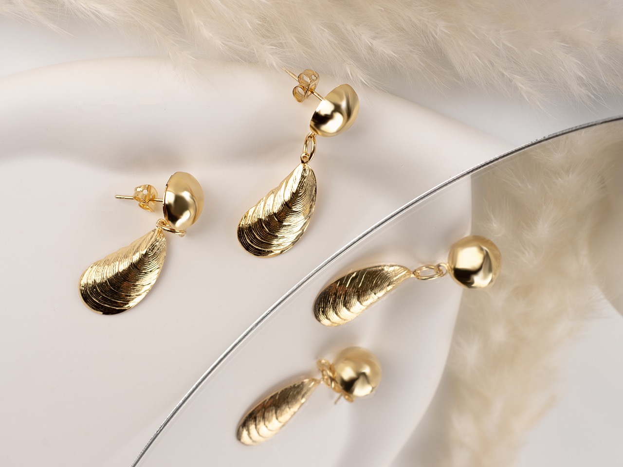 Dwie pary złotych kolczyków z motywem muszli na białym tle z elementami dekoracyjnymi z piór