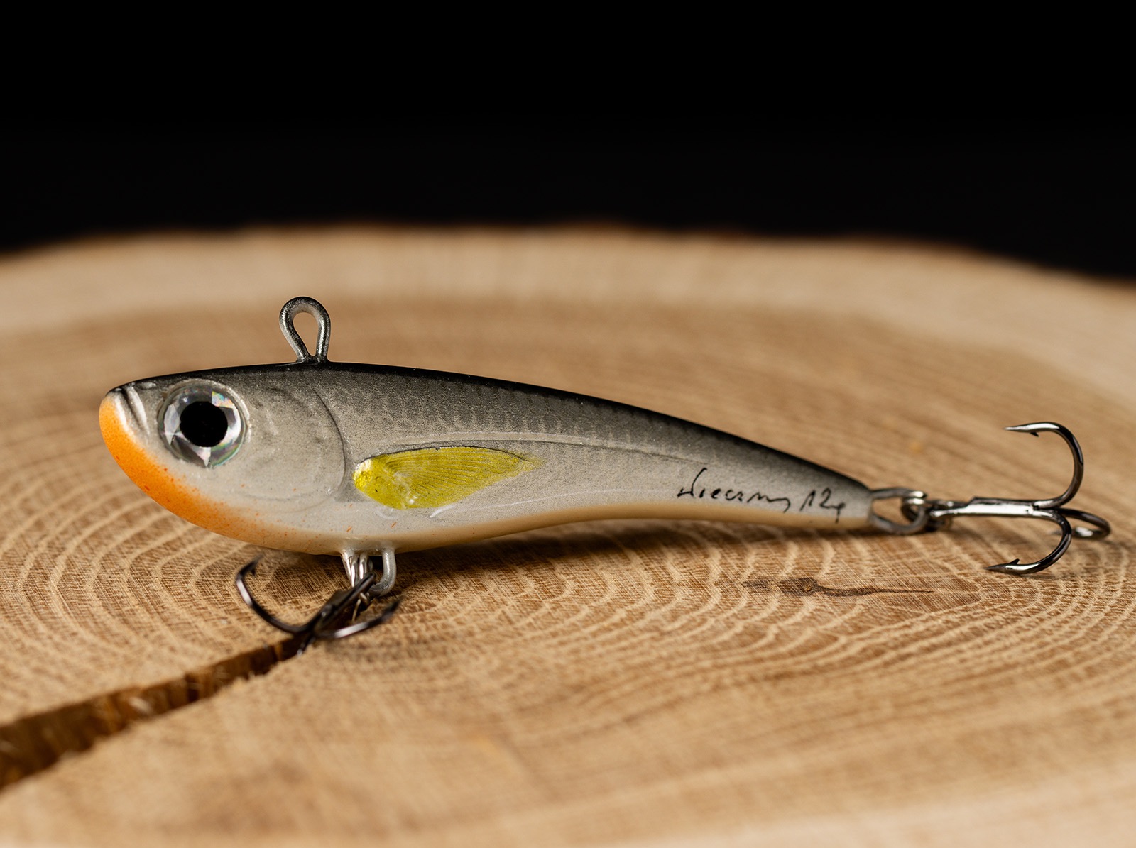 Szaro-pomarańczowa przynęta spinningowa z żółtym akcentem, leżąca na drewnianym blacie z widocznym podpisem 'Dreamy 124'.
