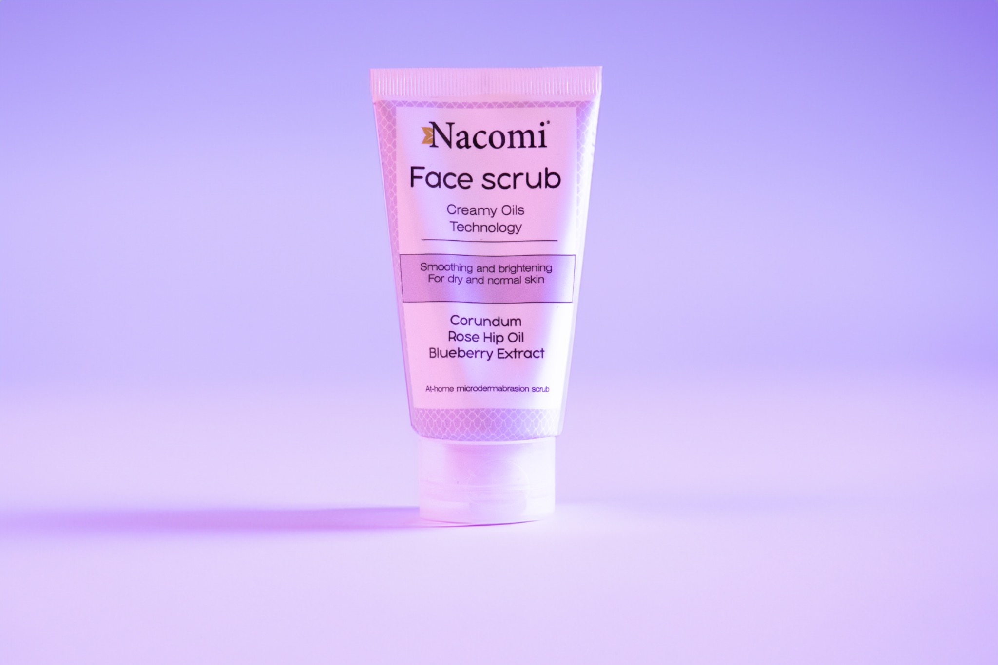 Biała tuba kremowego peelingu do twarzy Nacomi z ekstraktem z borówki i olejem z dzikiej róży na liliowym tle.