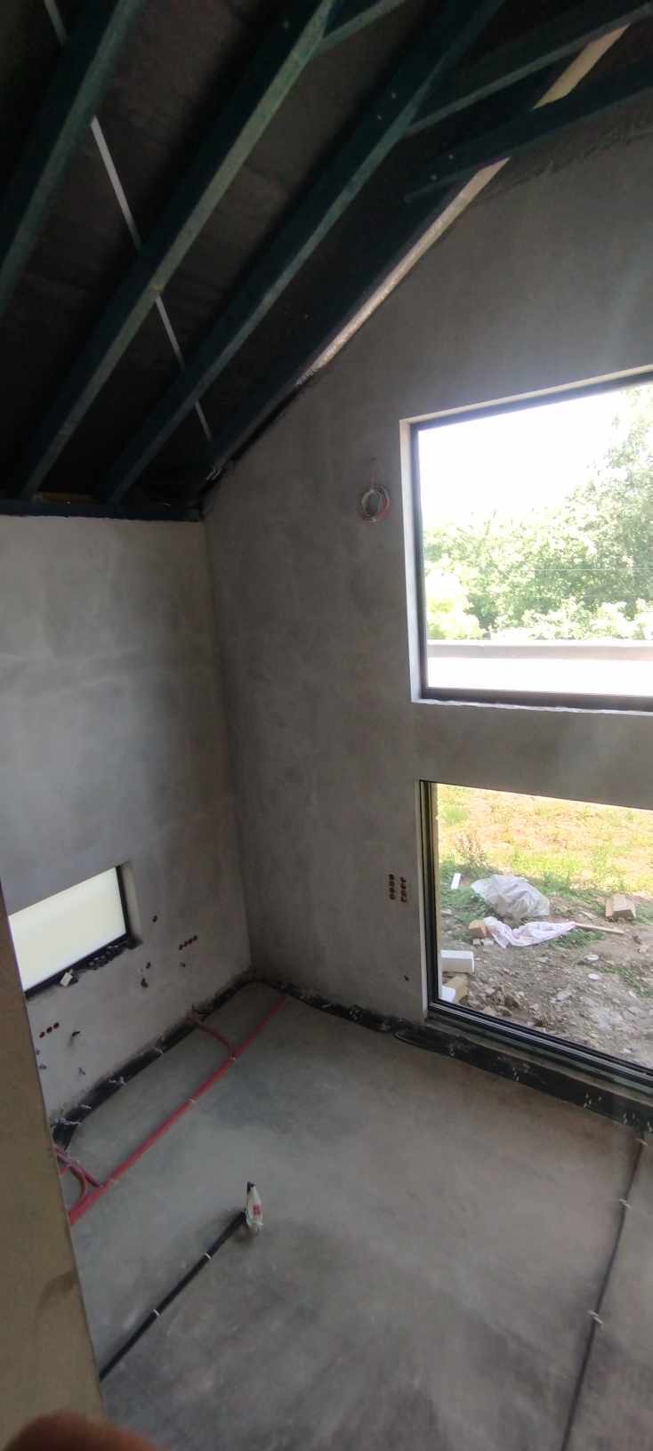 Pokój w stanie deweloperskim po nałożeniu gładzi, widoczne instalacje elektryczne w podłodze i surowy strop drewniany.