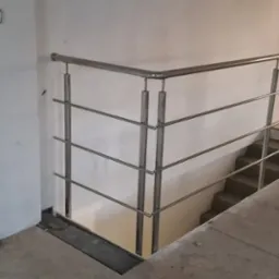 Nowoczesna balustrada ze stali nierdzewnej zamontowana przy schodach w surowym stanie, widoczny fragment pracownika w odblaskowej kamizelce.