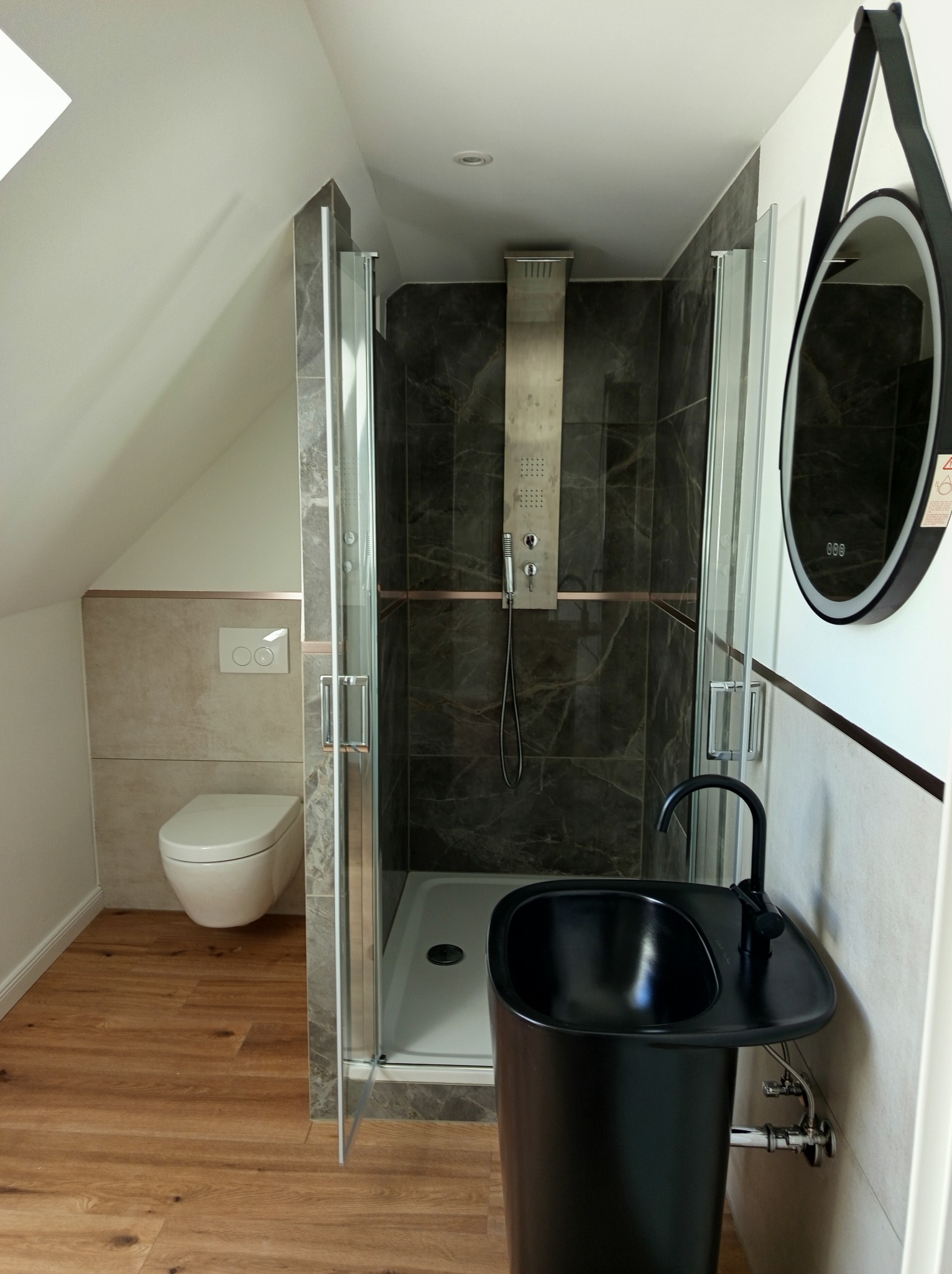 Nowoczesna łazienka na poddaszu w Gorlicach: kabina prysznicowa z deszczownicą, umywalka wolnostojąca i toaleta w zabudowie. Wykończenie w odcieniach szarości i drewna.