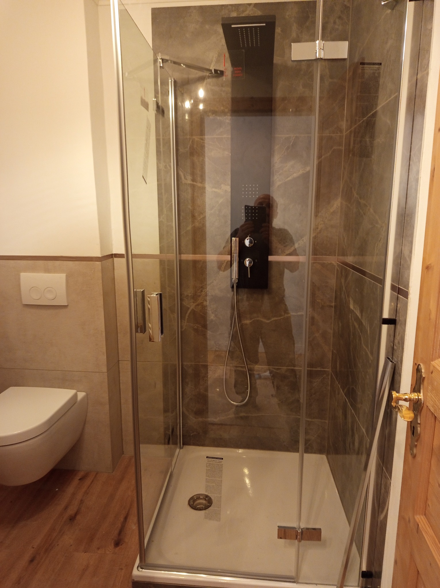 Nowoczesna kabina prysznicowa z deszczownicą i panelami imitującymi marmur, widoczna w wykończonej łazience z drewnopodobną podłogą.