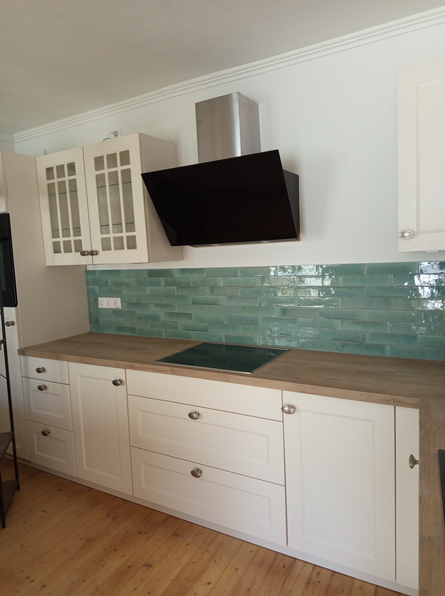 Biała zabudowa kuchenna z drewnianym blatem i turkusową glazurą. Widoczny czarny okap i płyta indukcyjna. Ujęcie na wykończoną kuchnię w mieszkaniu.