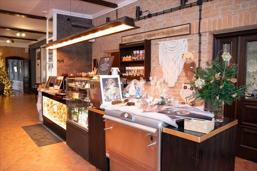 Wnętrze kawiarni z ladą, ekspozycją słodyczy, dekoracjami świątecznymi i makramami na ścianie z cegły.