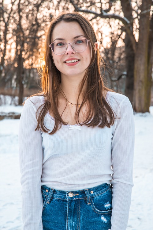 Portret młodej kobiety w okularach na tle zimowego krajobrazu z promieniami zachodzącego słońca