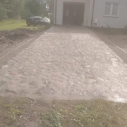 Ułożony z kamieni polnych podjazd do garażu z widocznym samochodem w tle.