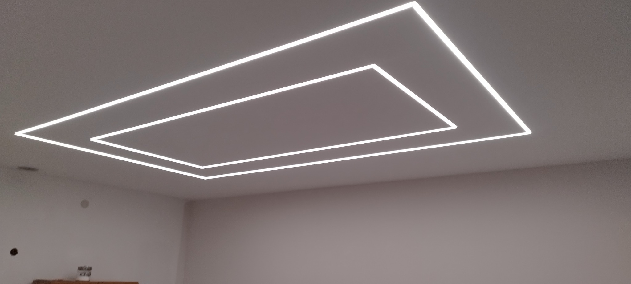 Nowoczesny sufit podwieszany z podświetleniem LED w kształcie dwóch prostokątów, tworzących efektowną kompozycję świetlną w minimalistycznym wnętrzu.