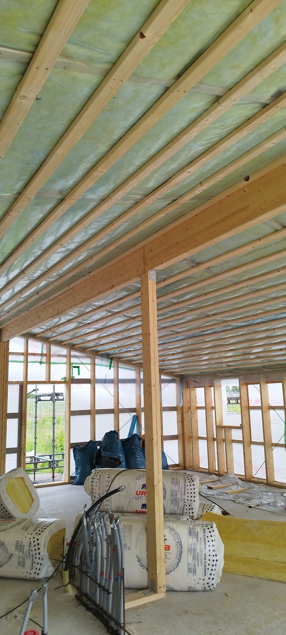 Wnętrze domu w konstrukcji szkieletowej, widoczne belki stropowe z folią, izolacja w rolkach i worki. Etap budowy domu szkieletowego.