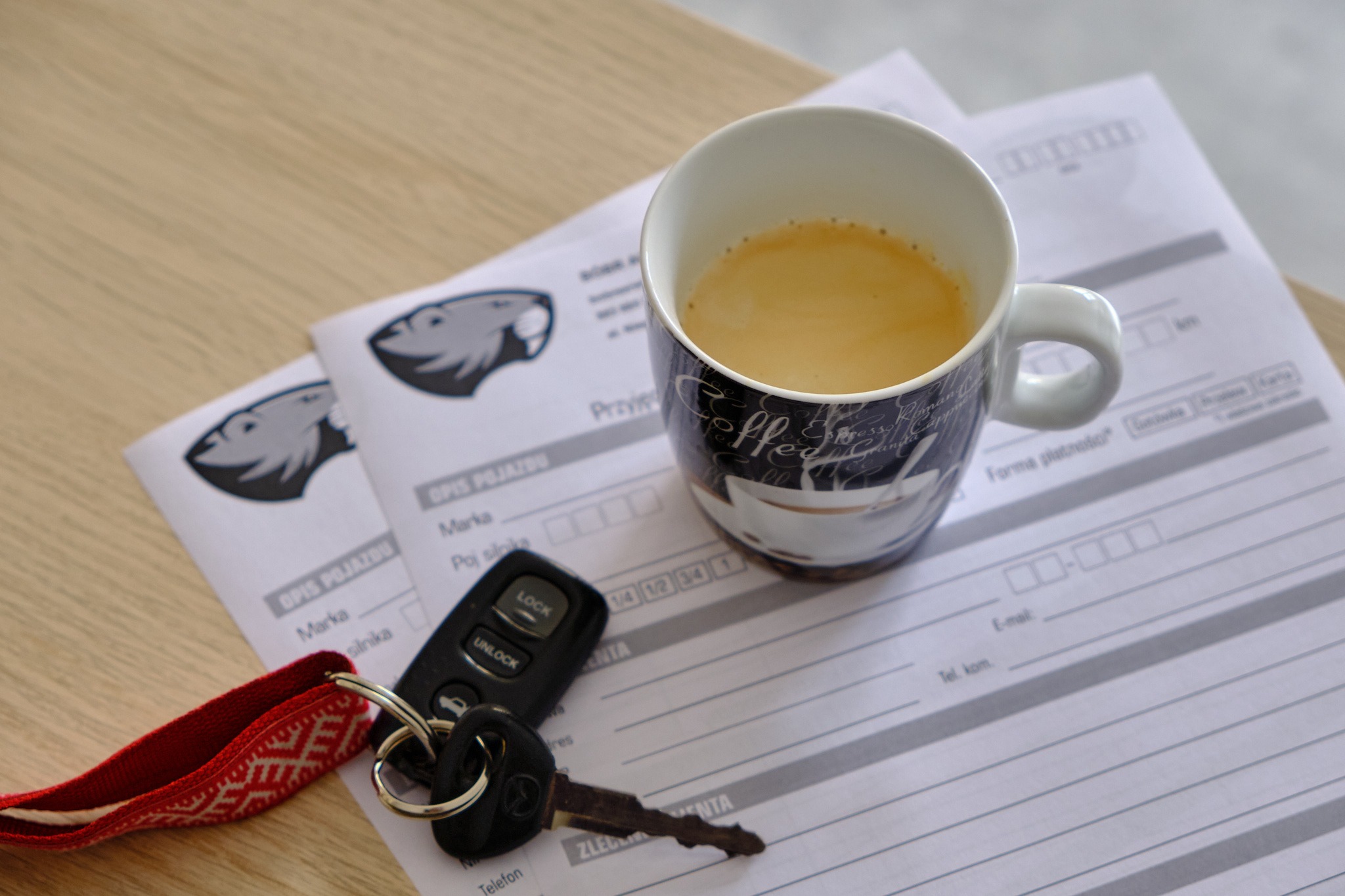 Formularz opisu pojazdu z kluczykami samochodowymi i kubkiem kawy na drewnianym biurku, sugerujący przerwę w pracy.