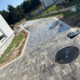 HUB-GARDEN-BRUK - Ułożona kostka brukowa w Sicienko tworzy elegancki podjazd do domu. Widoczny właz kanalizacyjny i obrzeża z jasnego kruszywa.