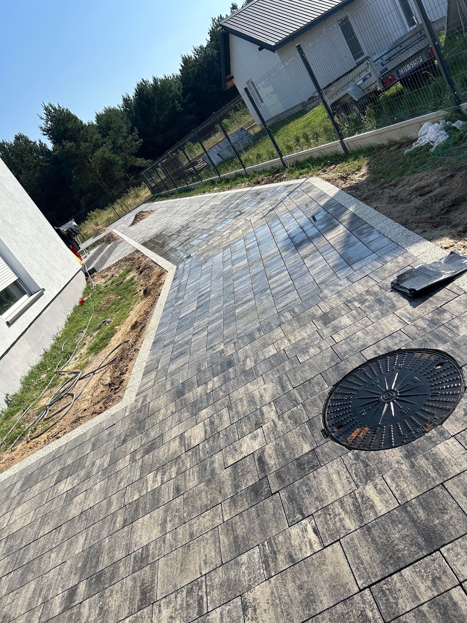 Ułożona kostka brukowa w Sicienko tworzy elegancki podjazd do domu. Widoczny właz kanalizacyjny i obrzeża z jasnego kruszywa.