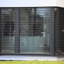 Nowoczesne okno z szarymi, poziomymi żaluzjami fasadowymi, zamontowane w białej elewacji budynku, widoczne z poziomu trawnika.